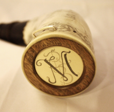 Butt Plug Medallion The client did not want a name on the horn. Preferring to have a monogram instead.  Since the body of the horn is covered with illustrations I inlaid a medallion of artificial Ivory in the turned elm  butt plug and engraved a monogram of my design with the initials RBM. I finished the horn with a sterling silver staple.