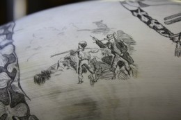 Minutemen Left Side Minutemen Left SideOn the left side of the eagle there is an illustration of two minutemen in the foreground. One with his back to us firing and the other reloading, his long coat flaring with the breeze.